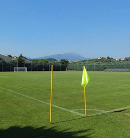 Tom fotbollsplan på Grand Prix Veronello Summer Trophy-turneringen, med grönska och berg i bakgrunden.