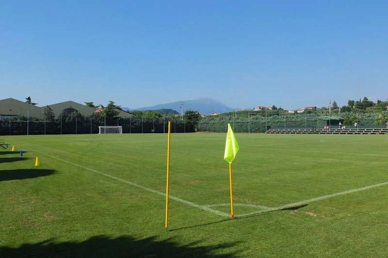 Terrain de football vide au tournoi Grand Prix Veronello Summer Trophy, avec verdure et montagnes en arrière-plan.