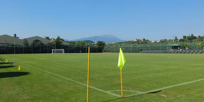 Campo de fútbol vacío en el torneo Grand Prix Veronello Summer Trophy, con vegetación y montañas de fondo.