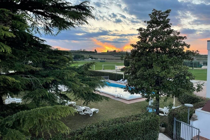 Football field and pool with sun loungers at Veronello sports resort, Italy, with sunset in the background.