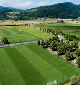 Fodboldbaner ved Grand Prix Čatež Summer Trophy-turneringen, omgivet af træer med bjerge i baggrunden.