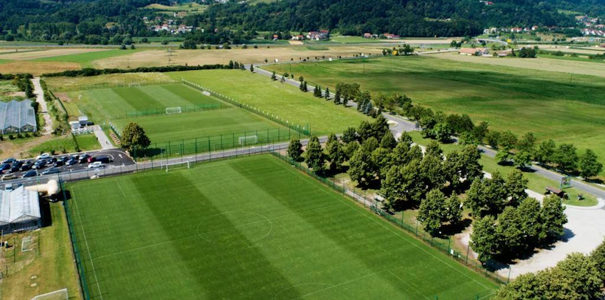 Football fields at Grand Prix Čatež Summer Trophy tournament surrounded by trees with mountains in the background.