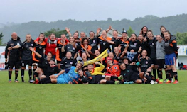 Женская футбольная команда празднует на турнире Tournoi National Feminin, позирует с широкими улыбками на футбольном поле.