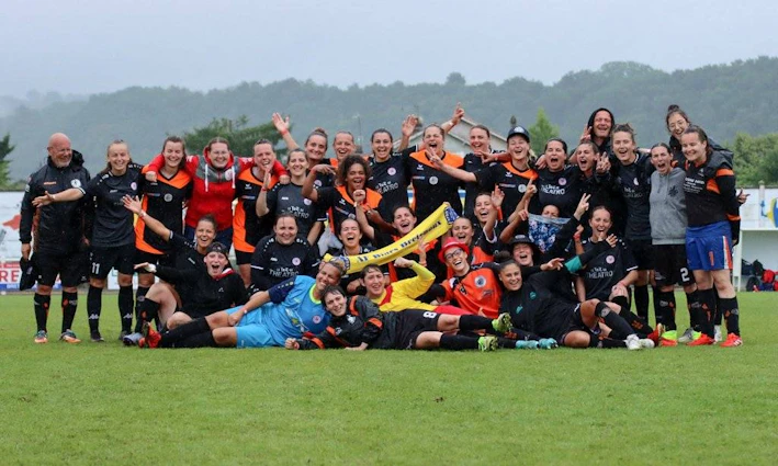 Η γυναικεία ποδοσφαιρική ομάδα γιορτάζει στο τουρνουά Tournoi National Feminin, ποζάροντας με μεγάλα χαμόγελα στο γήπεδο.