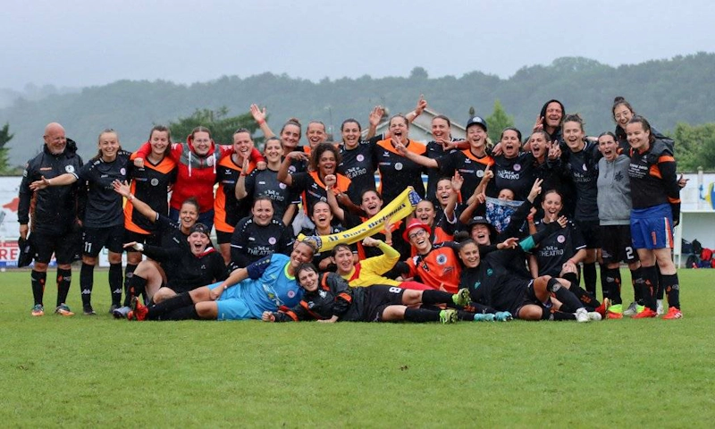 Tournoi National Femininトーナメントで祝う女子サッカーチームが、サッカー場で笑顔を見せています。