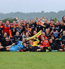 Women's football team celebrating at the Tournoi National Feminin tournament, posing with wide smiles on the football field.