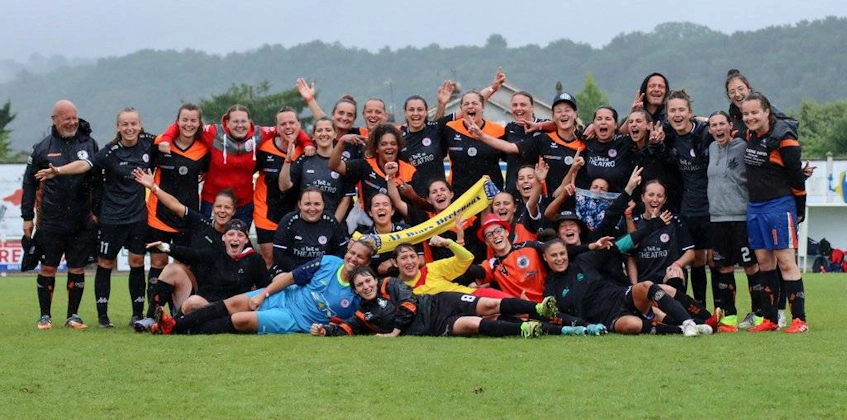 Women's football team celebrating at the Tournoi National Feminin tournament, posing with wide smiles on the football field.