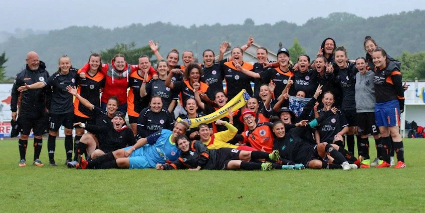 Drużyna piłki nożnej kobiet świętuje na turnieju Tournoi National Feminin, pozując z szerokimi uśmiechami na boisku.