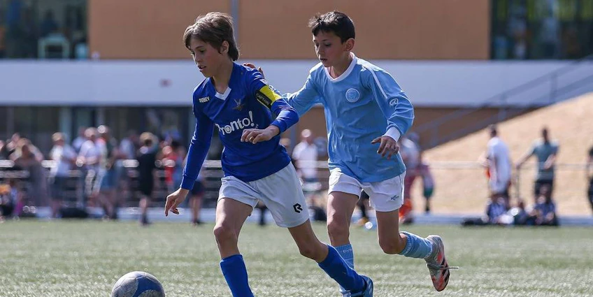 Hermes DVS International Youth Cup -turnauksen jalkapallo-ottelu, jossa kaksi nuorta pelaajaa taistelevat pallosta.