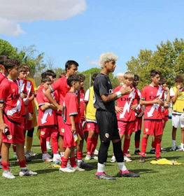 Drużyna piłkarska w czerwonych strojach na turnieju U15 Madrid Youth Cup Summer, młodzi zawodnicy przygotowują się do meczu.