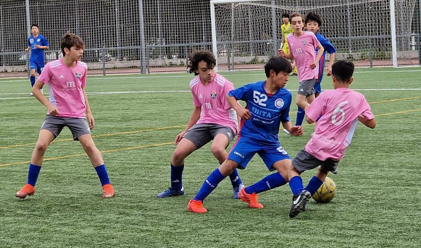 Jucători care concurează pentru minge la U15 Madrid Youth Cup pe un teren verde
