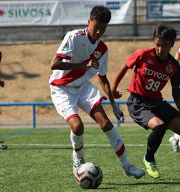 Fodboldkamp ved U18 Madrid Youth Cup Summer-turneringen, spillere i røde og hvide uniformer kæmper om bolden.