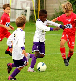 Mecz piłki nożnej na turnieju Dufour International Cup, zawodnicy w białych i czerwonych strojach walczą o piłkę.