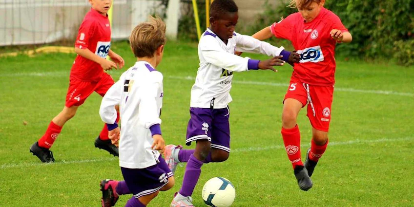 Fotbollsmatch vid Dufour International Cup-turneringen, spelare i vita och röda uniformer kämpar om bollen.