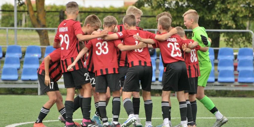 Fotbollslag i röda och svarta uniformer på Summer Finest League-turneringen, spelare samlade i en cirkel.