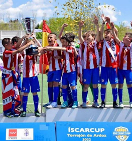 Jovens futebolistas com uniformes listrados em vermelho e branco comemoram a vitória com um troféu no torneio de futebol ÍscarCup.