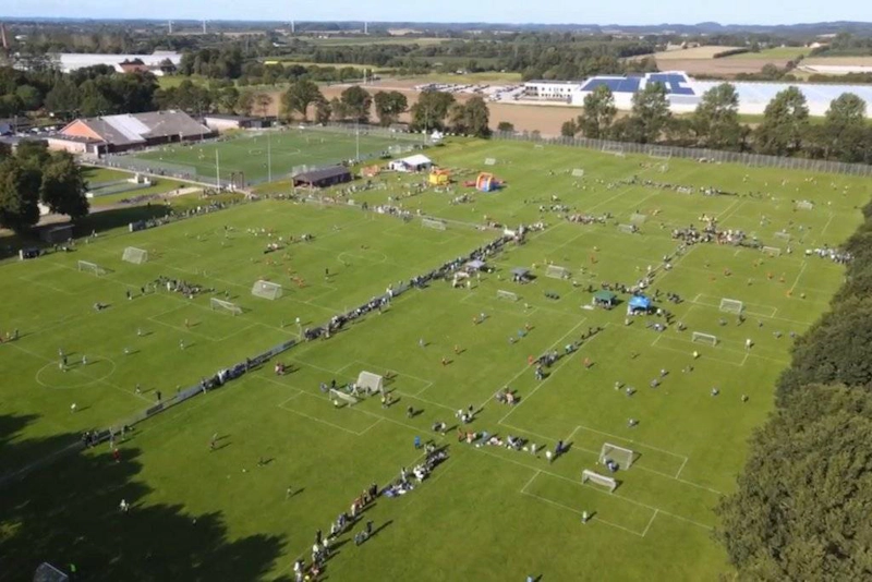 Вид с воздуха на футбольный турнир BBB Cup с множеством полей и участников.